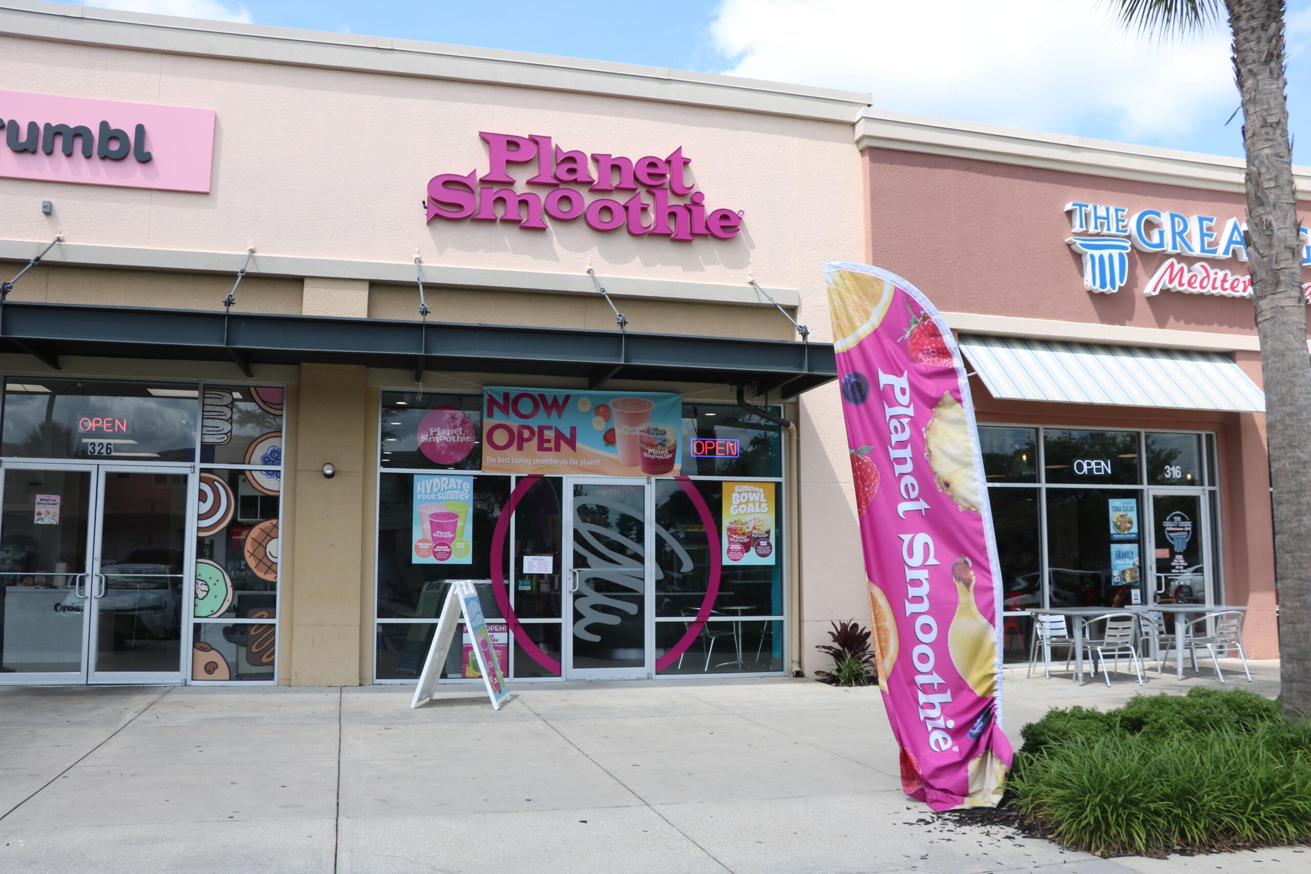 Exterior view of a shopping plaza. Three restaurants stand next to eachother, Crumbl, Planet Smoothie and The Great Mediterranean.