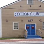 Beige wooden building with blue double doors, wreaths, and a sign reading COTTON CLUB Museum and Cultural Center; address 837.