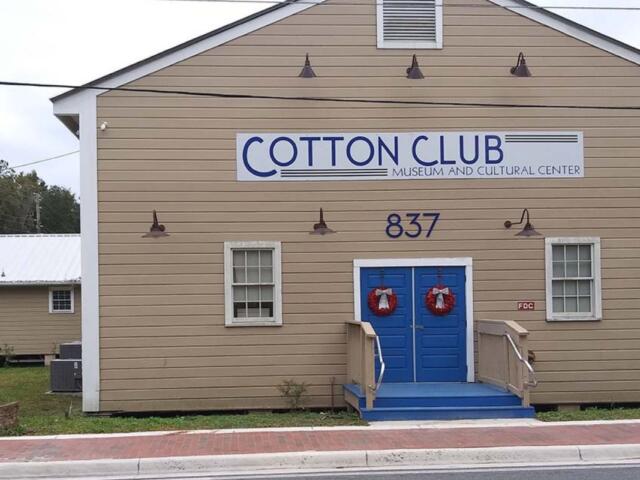 Beige wooden building with blue double doors, wreaths, and a sign reading COTTON CLUB Museum and Cultural Center; address 837.