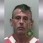 A mugshot of a man in an orange and white striped jumpsuit.