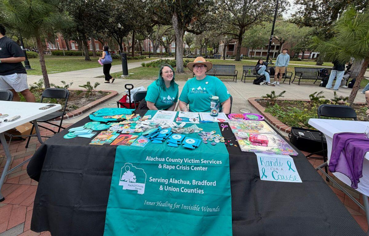 A colored image of two people in light blue shirts smiling behind a booth.