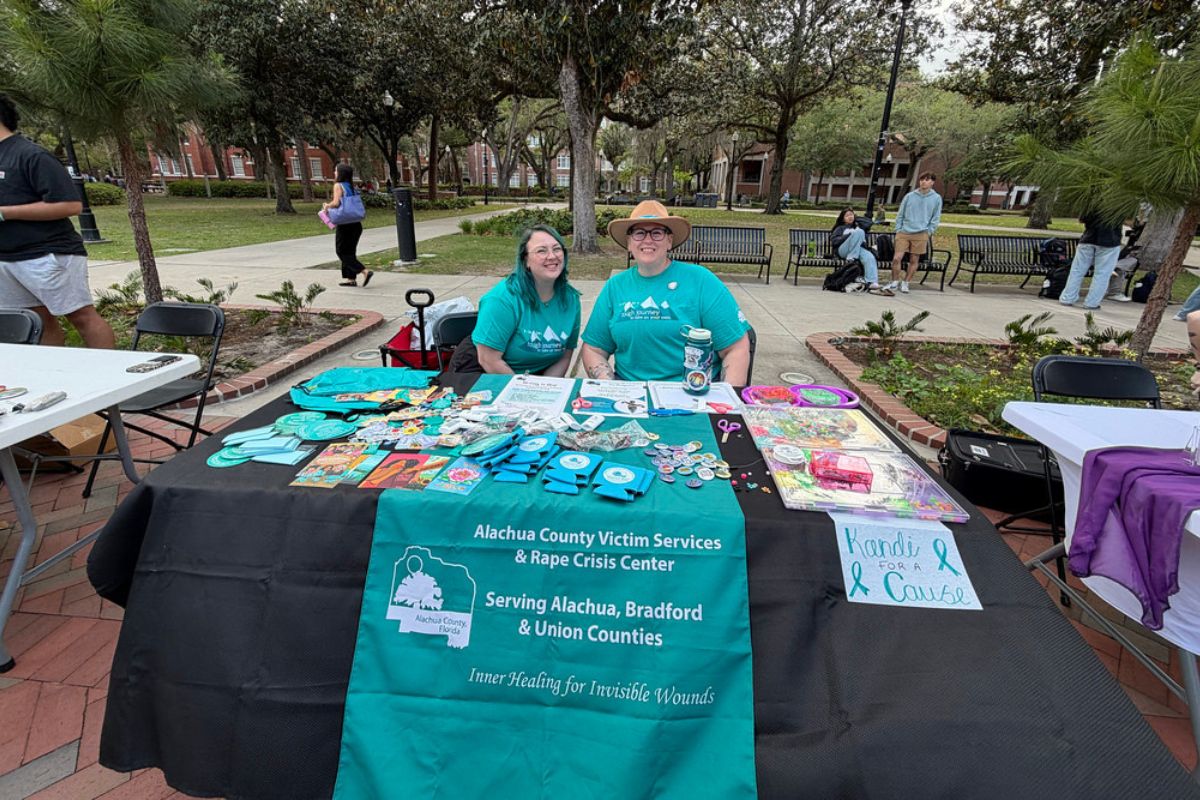 A colored image of two people in light blue shirts smiling behind a booth.