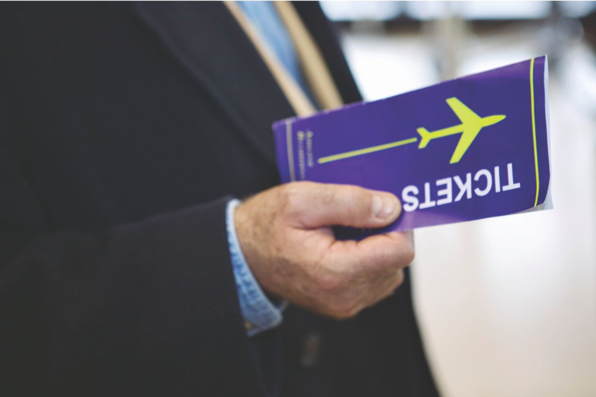 A colored image of a man in a suit holding a blue airline ticket.