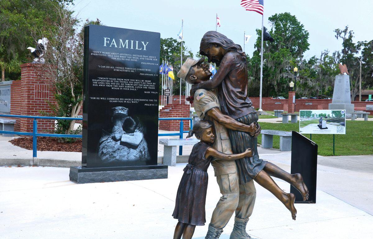 A statue of a soldier carrying his wife while a young girl hugs them from behind.
