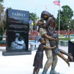 A statue of a soldier carrying his wife while a young girl hugs them from behind.
