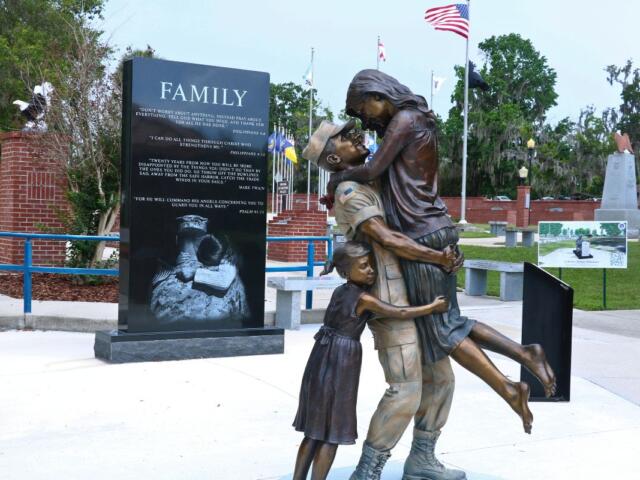A statue of a soldier carrying his wife while a young girl hugs them from behind.