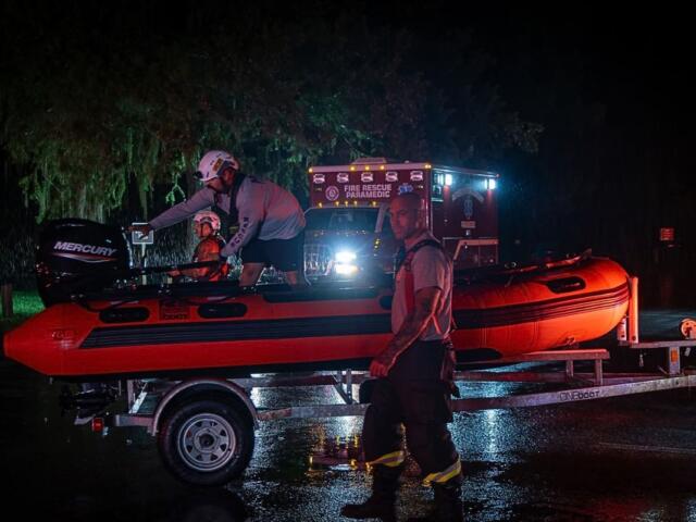 A image of a rescue boat on a boat trailer in front of an ambulance at nighttime.
