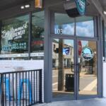 The exterior of a restaurant features signs reading, "Big Hammock Brewery & Bites." Outdoor seating lines the walls on a sidewalk with a small, black fence next to the entrance.