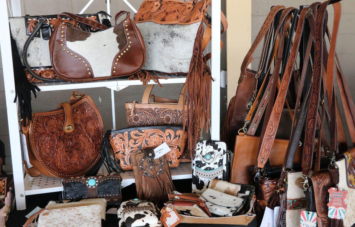 Display of brown leather bags and purses with tooled patterns on a store rack. Various shapes and fringe details visible for sale.