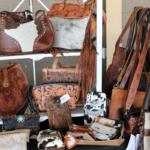 Display of brown leather bags and purses with tooled patterns on a store rack. Various shapes and fringe details visible for sale.