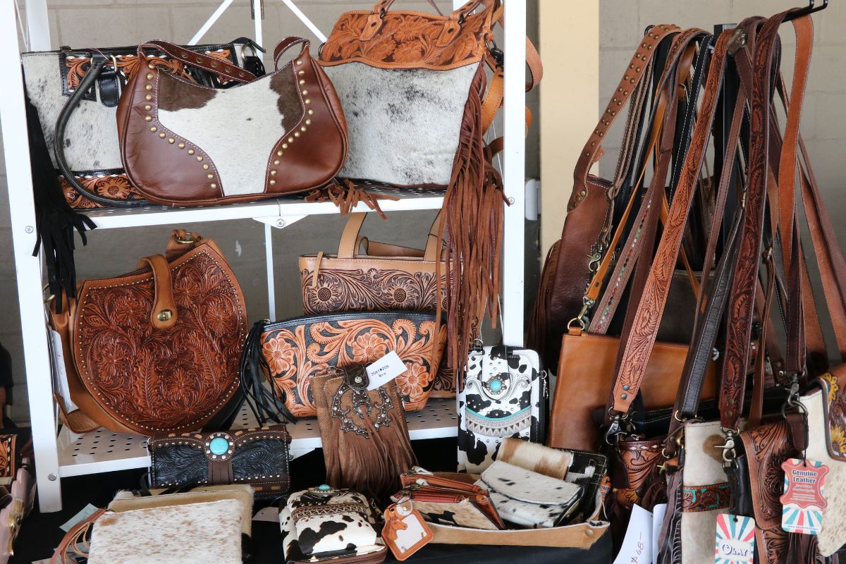 Display of brown leather bags and purses with tooled patterns on a store rack. Various shapes and fringe details visible for sale.