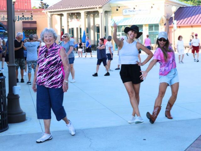 Three ladies pose together in a shopping plaza with line-dancing and athletic outfits.