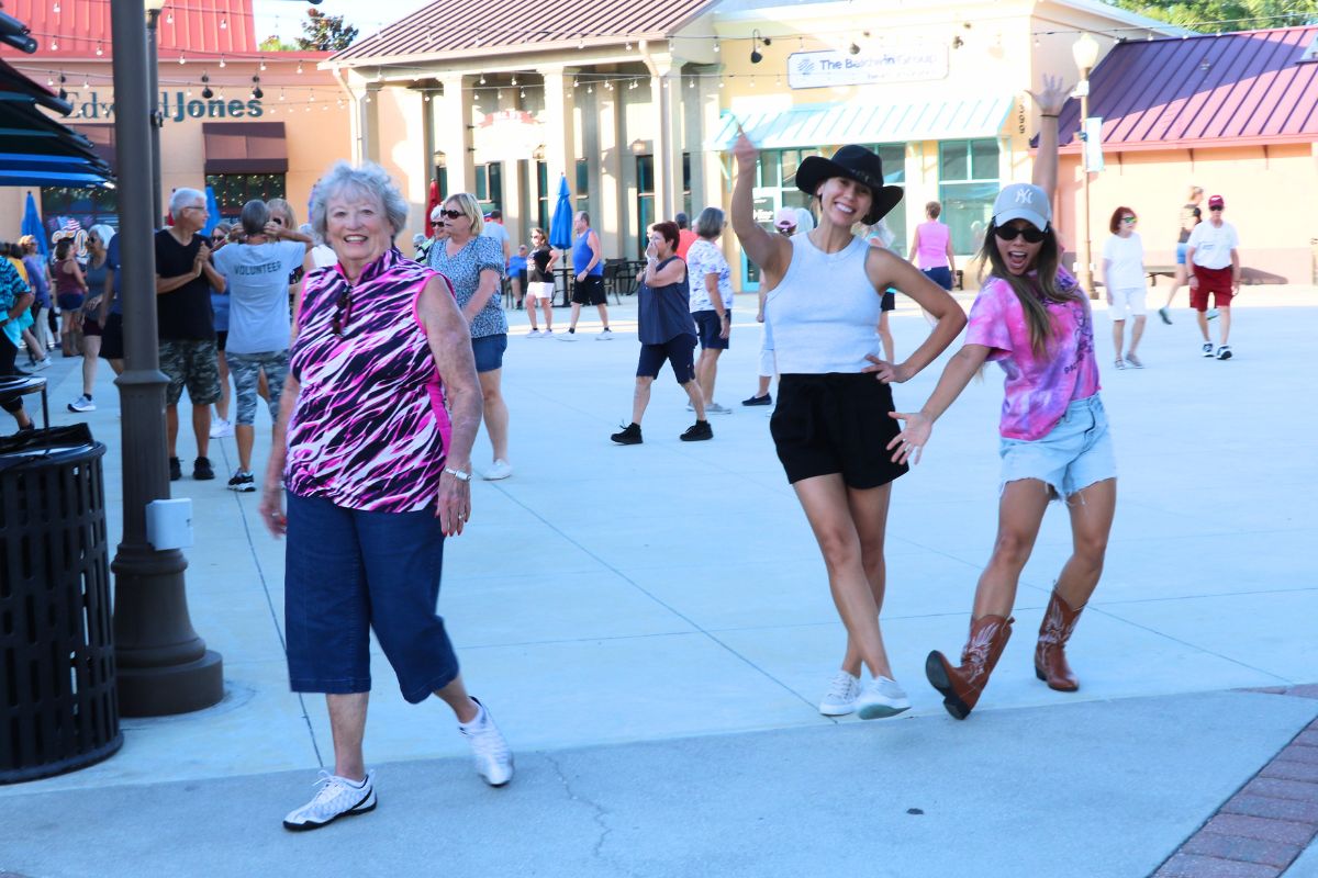 Three ladies pose together in a shopping plaza with line-dancing and athletic outfits.