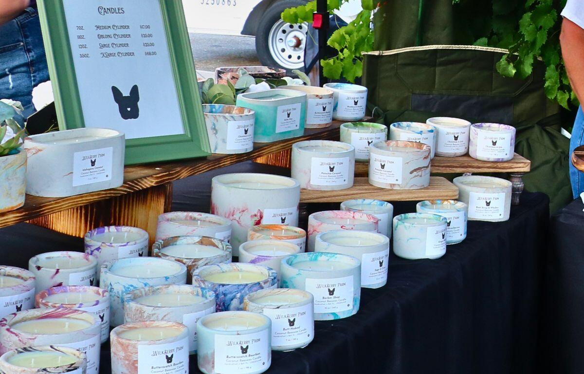 Rows of colorful marbled candles in white jars arranged on a wooden display at an outdoor market stall.