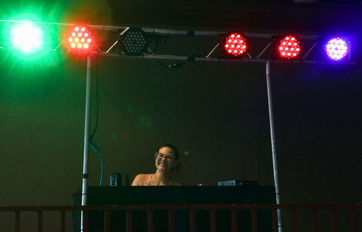 A DJ stands behind a tall table. Large red, green and blue lights flash above her.