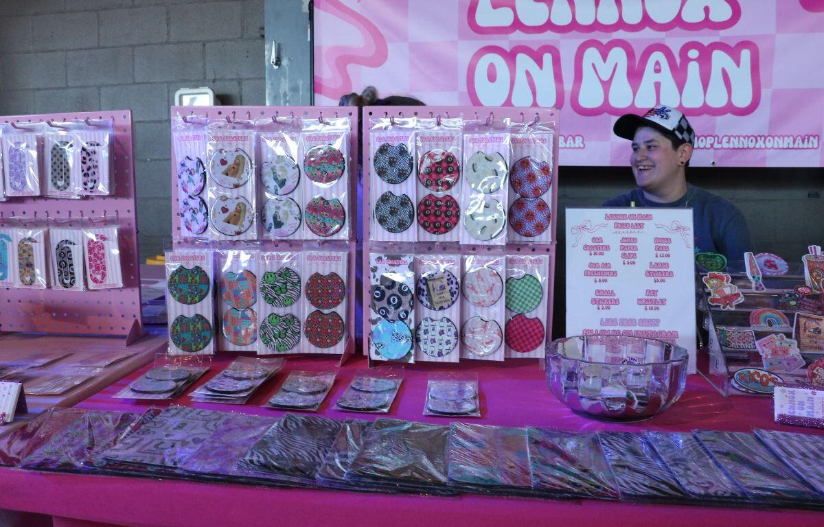 Vendor booth selling colorful circular nail art patches and accessories on a bright pink table at a fairground stall.