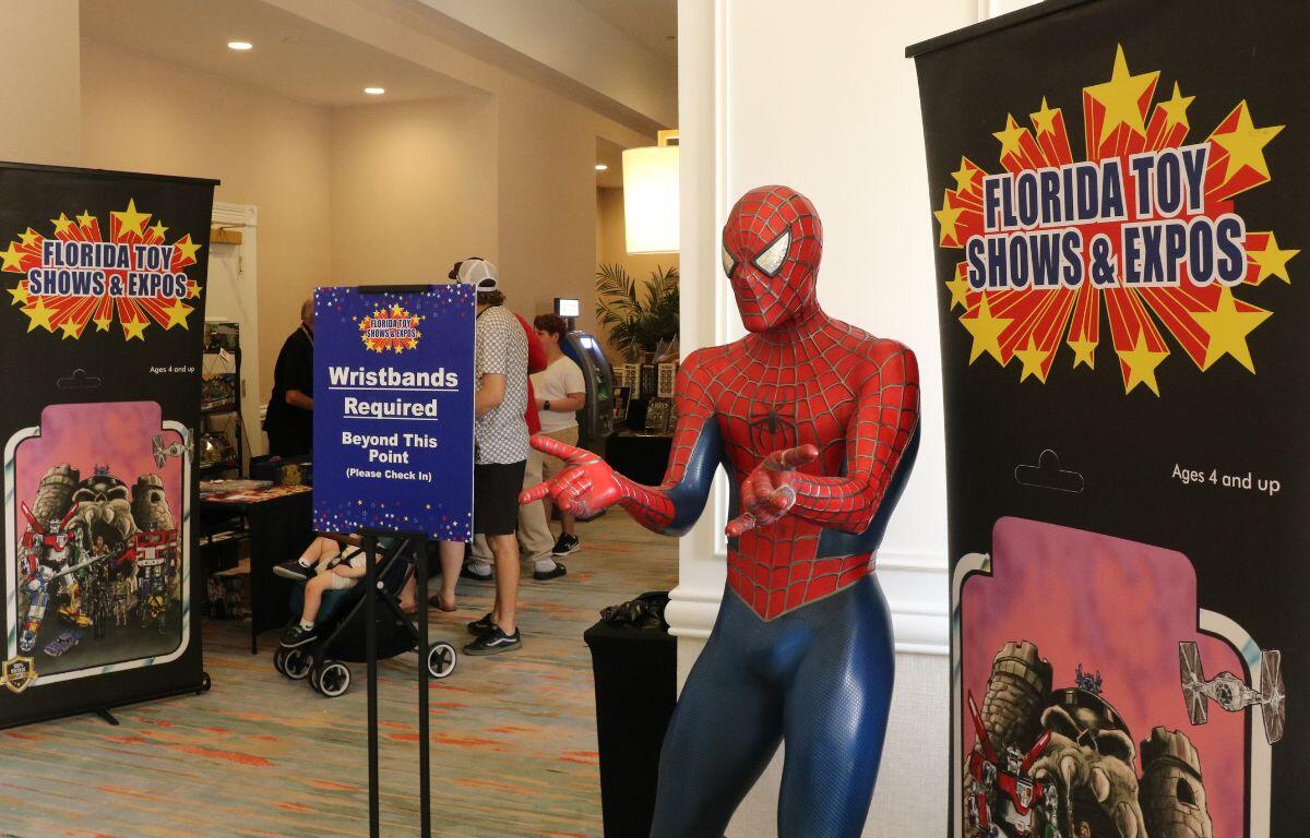 A large Spiderman statue stands in an open hallway with tall, black banners reading, "Florida Toy Shows & Expos."