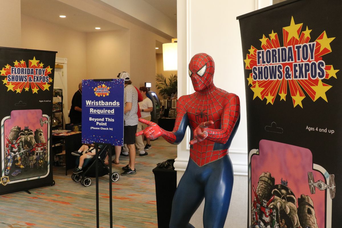 A large Spiderman statue stands in an open hallway with tall, black banners reading, "Florida Toy Shows & Expos."