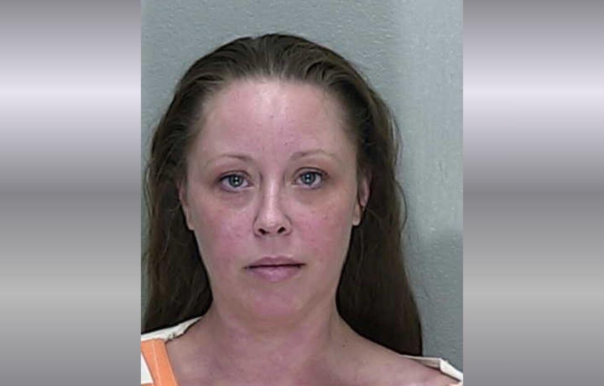 A mugshot of a woman with brown hair in a orange and white striped jumpsuit.