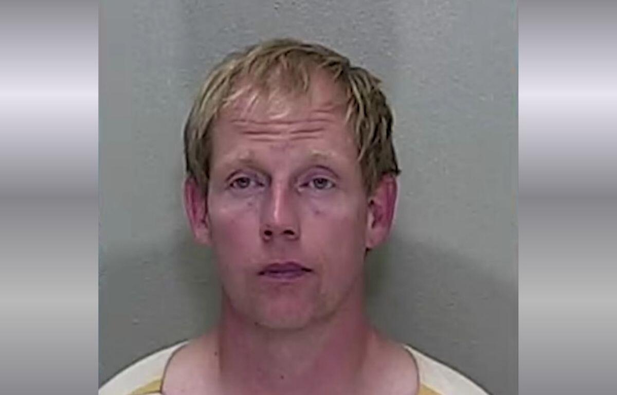 A mugshot of a man with short blonde hair in an orange and white striped jumpsuit.