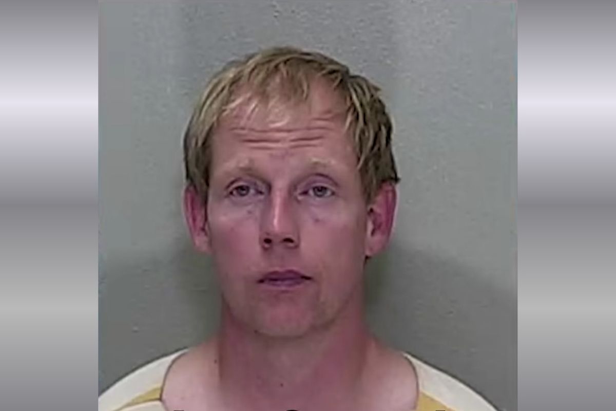 A mugshot of a man with short blonde hair in an orange and white striped jumpsuit.