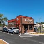 A colored image of a brown and orange coffee shop with an occupied drive-thru.