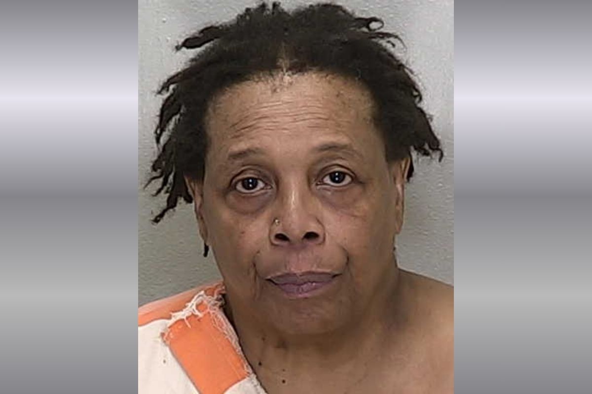 A mugshot of a black woman with short hair in an orange and white striped jumpsuit against a gray background.