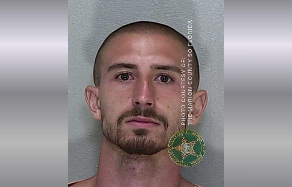 A mugshot of a man with a mustache and goatee with buzzed hair in a jumpsuit.