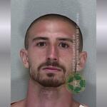 A mugshot of a man with a mustache and goatee with buzzed hair in a jumpsuit.
