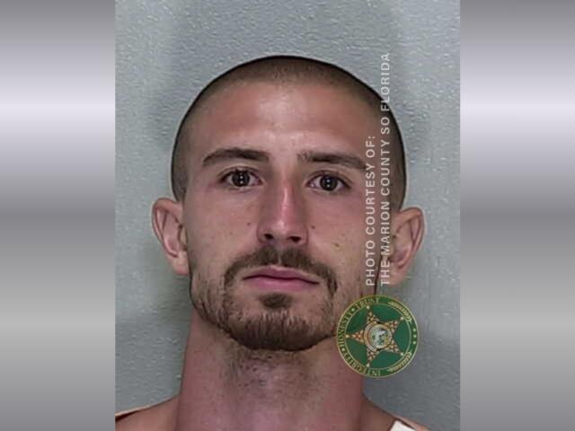 A mugshot of a man with a mustache and goatee with buzzed hair in a jumpsuit.