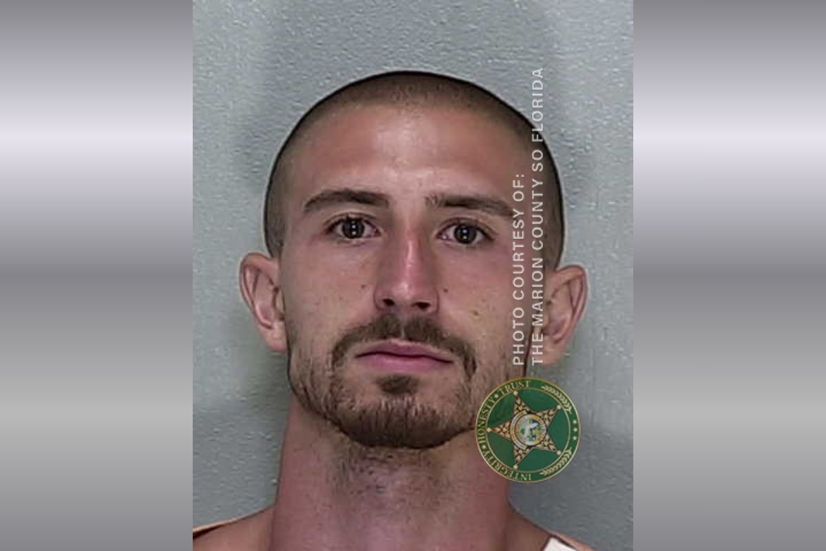 A mugshot of a man with a mustache and goatee with buzzed hair in a jumpsuit.