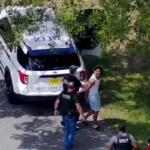 A still for drone surveillance footage of a man in a white tank top and blue shorts being arrested by law enforcement officers.