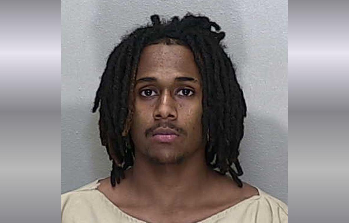 A mugshot of a African American man with shoulder-length black dreadlocks in a beige jumpsuit.