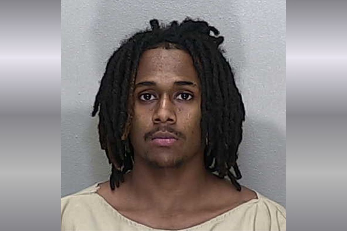 A mugshot of a African American man with shoulder-length black dreadlocks in a beige jumpsuit.