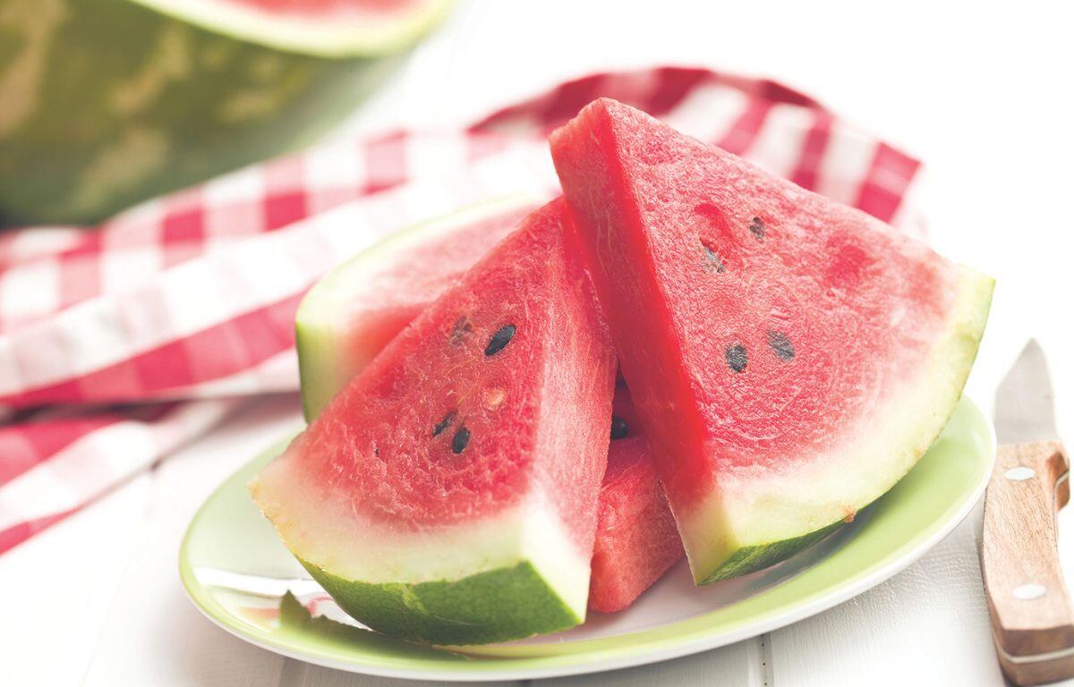 A colored picture of sliced watermelon on a plate against a white and red checkered tablecloth.