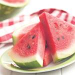 A colored picture of sliced watermelon on a plate against a white and red checkered tablecloth.