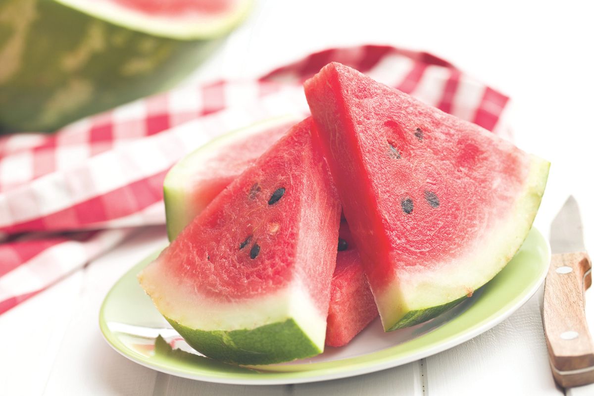 A colored picture of sliced watermelon on a plate against a white and red checkered tablecloth.