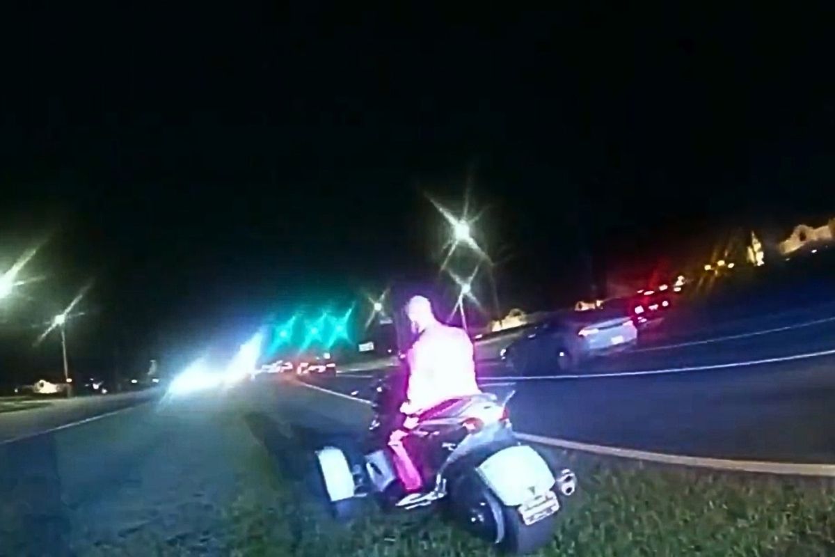 A still from body cam footage of a man in a pink business suit sitting on a silver trike.