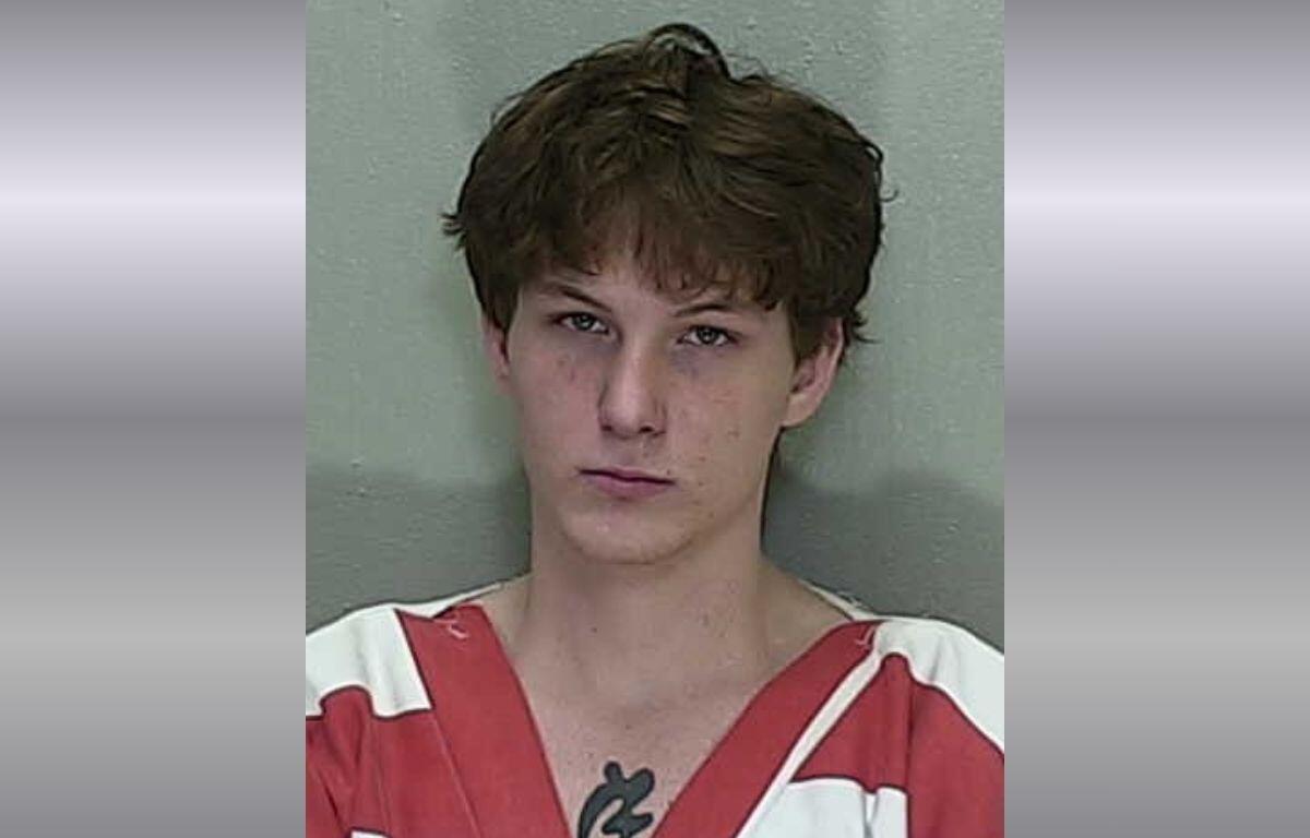 A mugshot of a young man with short brown hair in an orange and white striped jumpsuit.