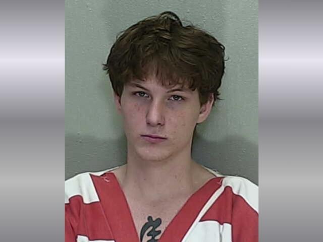 A mugshot of a young man with short brown hair in an orange and white striped jumpsuit.