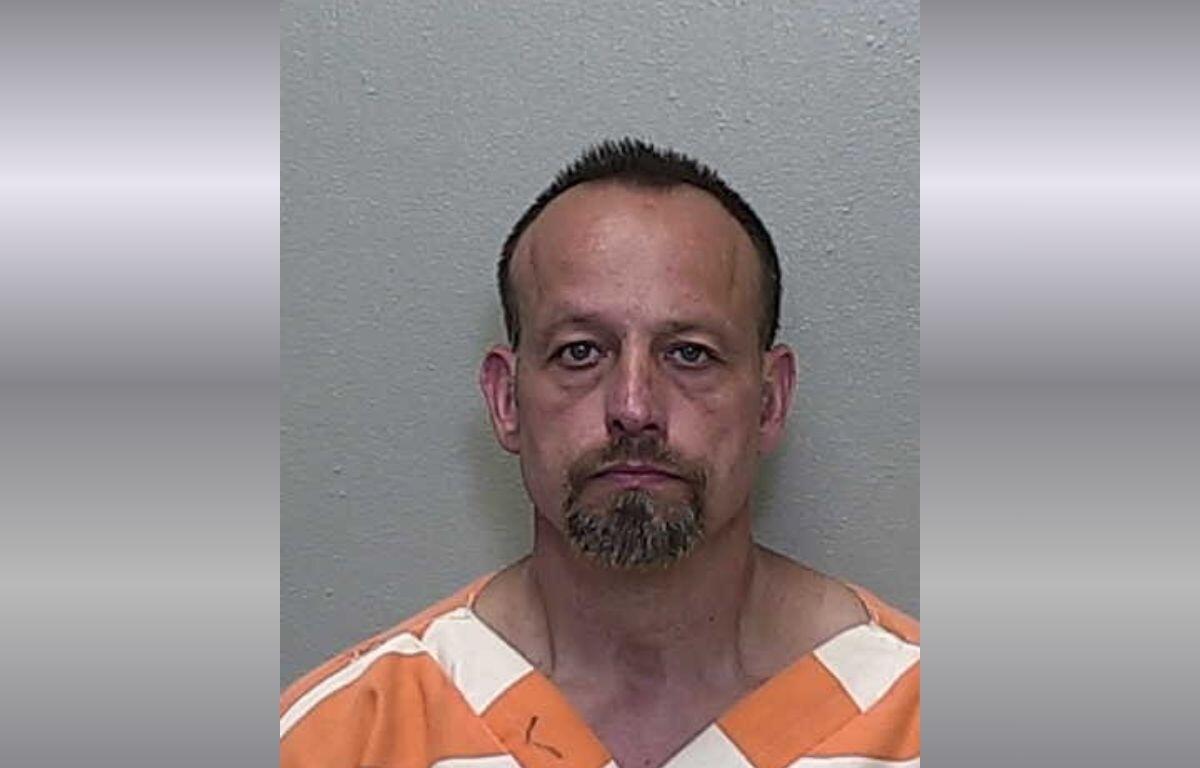 A white man with short hair in an orange and white striped jumpsuit.