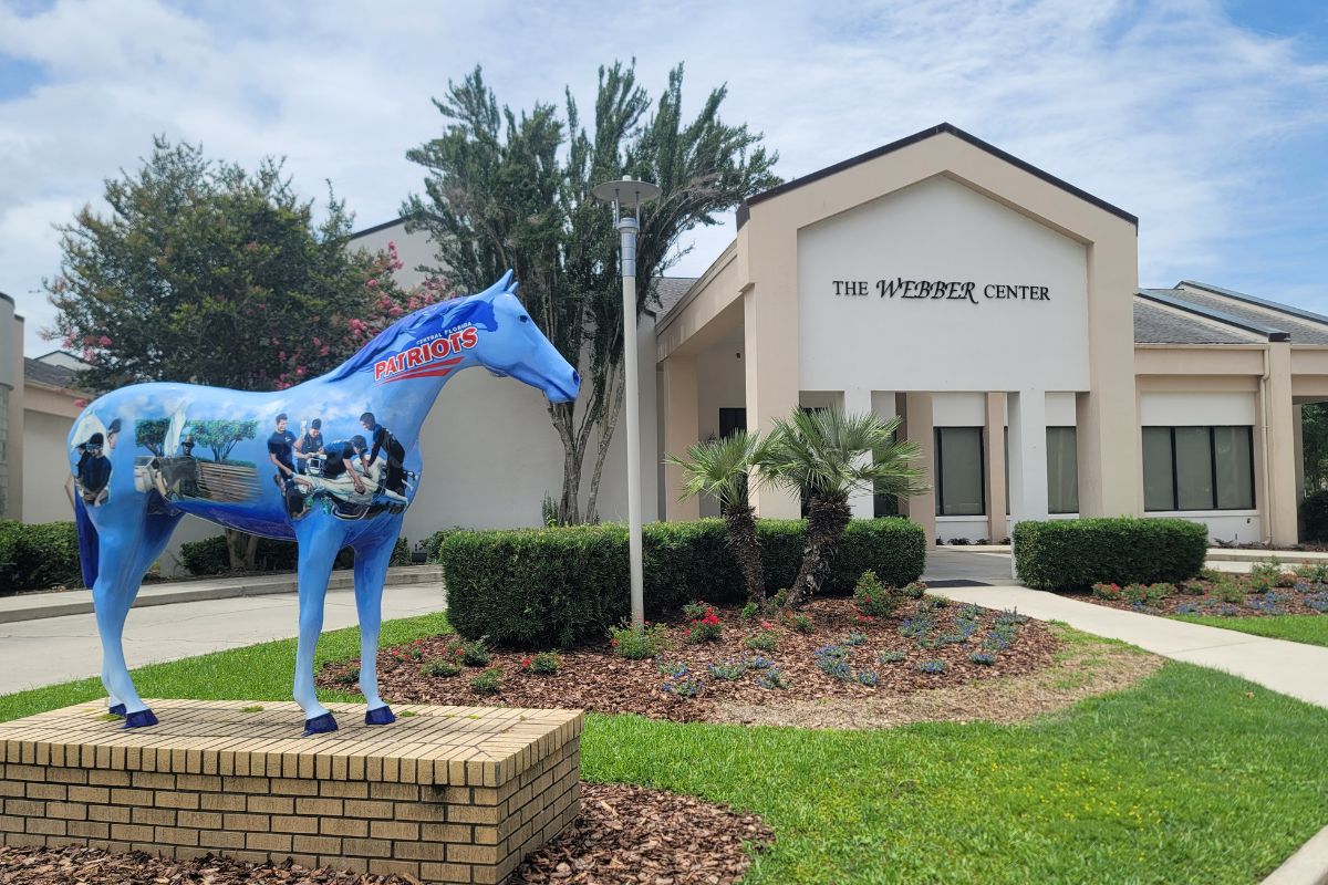 A large horse statue with painted depictions of medical students stands in front of a large conference center. Over the entrance of the center reads, "The Webber Center."