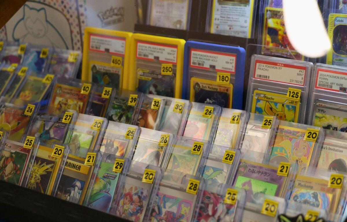 Display case filled with Pokémon trading cards in protective sleeves with yellow price tags.