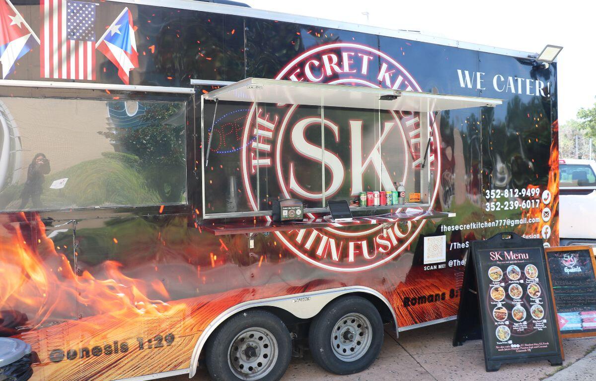 Food truck with 'SECRET KITCHEN' logo and 'We Cater!' text, service window open with condiments on the counter.