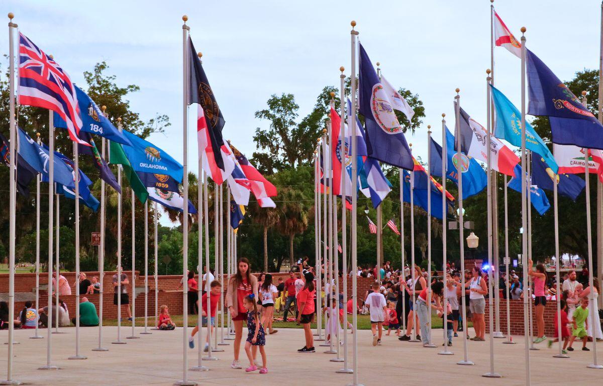 People walk through a courtyard with flags in a Veteran Memorial Park.