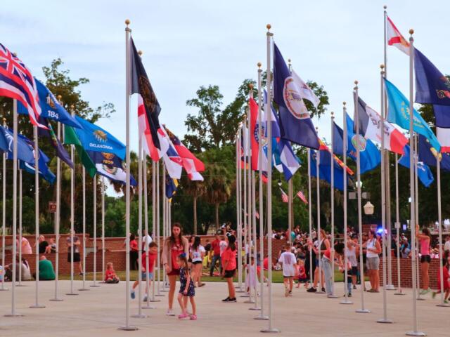 People walk through a courtyard with flags in a Veteran Memorial Park.