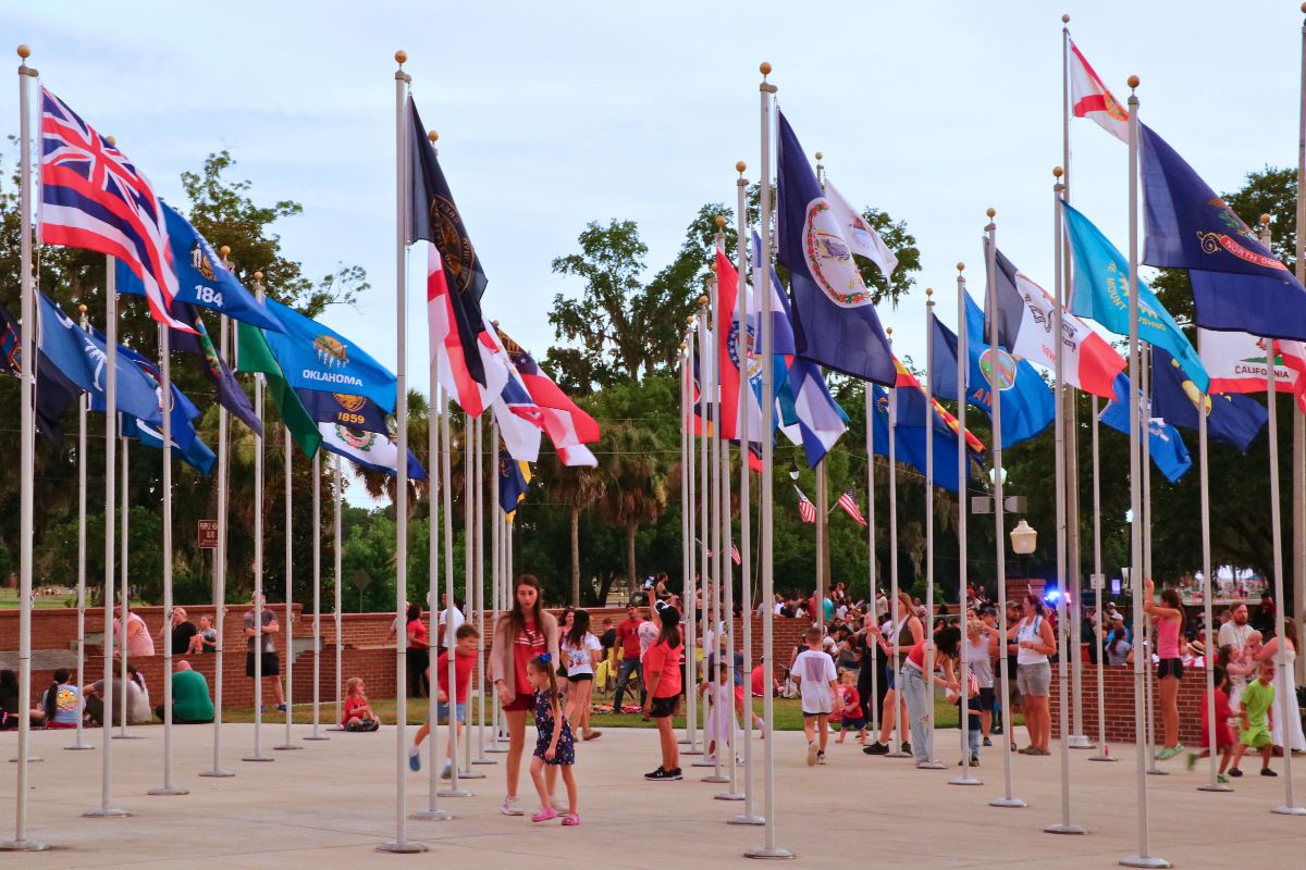 People walk through a courtyard with flags in a Veteran Memorial Park.