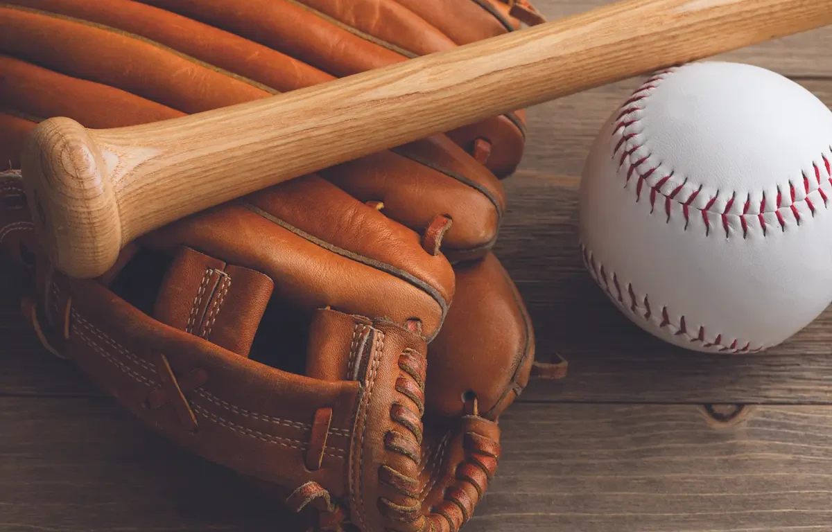 Baseball glove with a wooden bat resting on a wooden surface beside a white baseball.