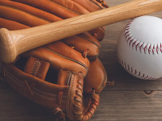 Baseball glove with a wooden bat resting on a wooden surface beside a white baseball.