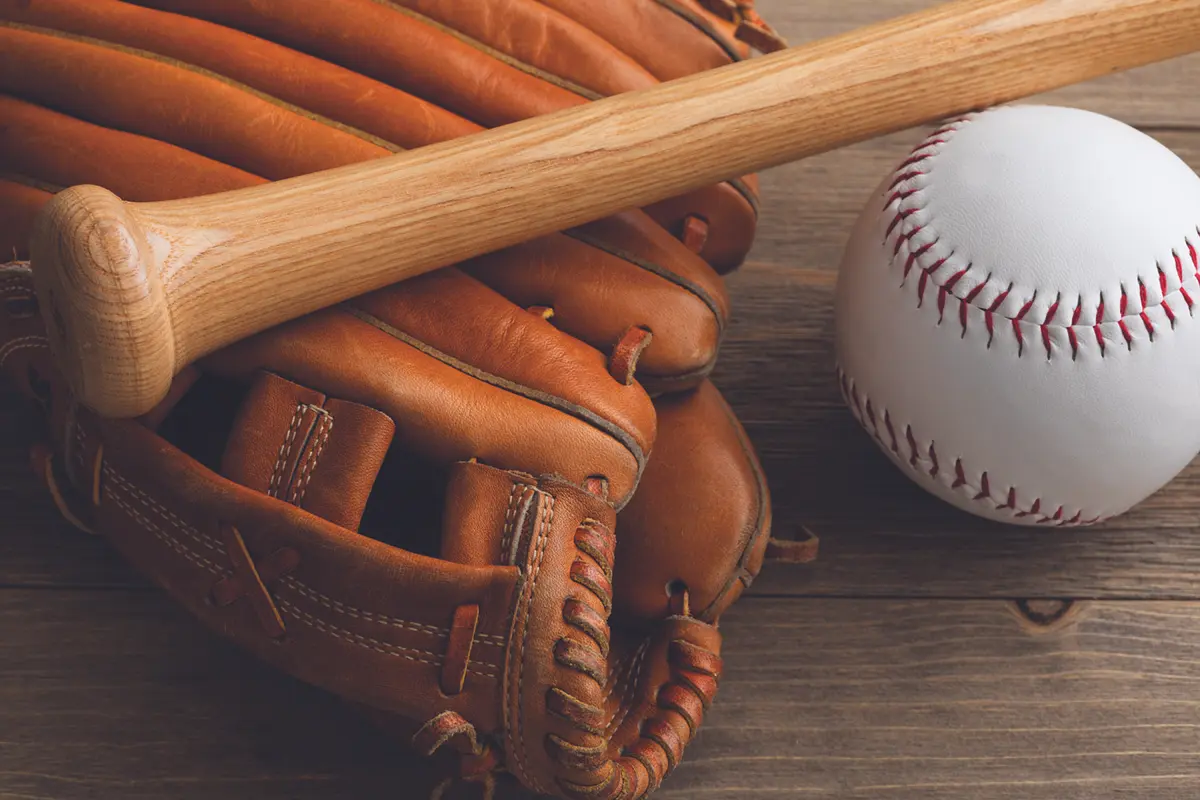 Baseball glove with a wooden bat resting on a wooden surface beside a white baseball.